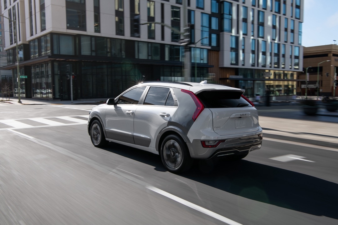 Vue 3/4 arrière du Kia Niro EV 2025 roulant sur un boulevard en ville.