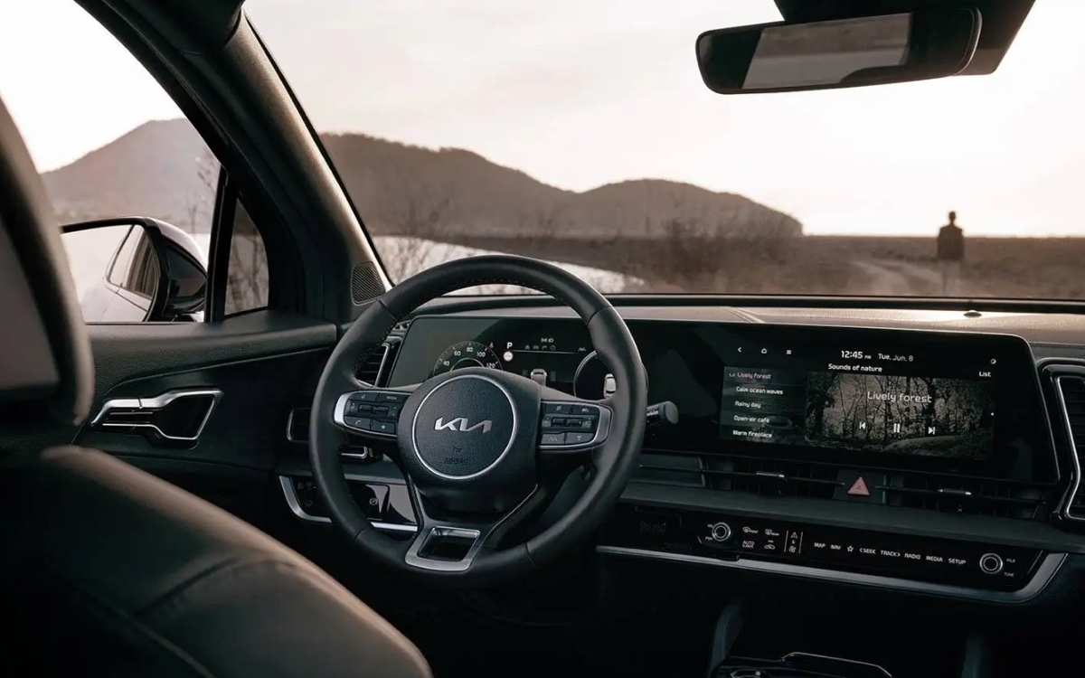 Vue intérieure du Kia Sportage 2025 mettant en valeur le volant, l'écran tactile central et l'ambiance apaisante avec fond naturel.